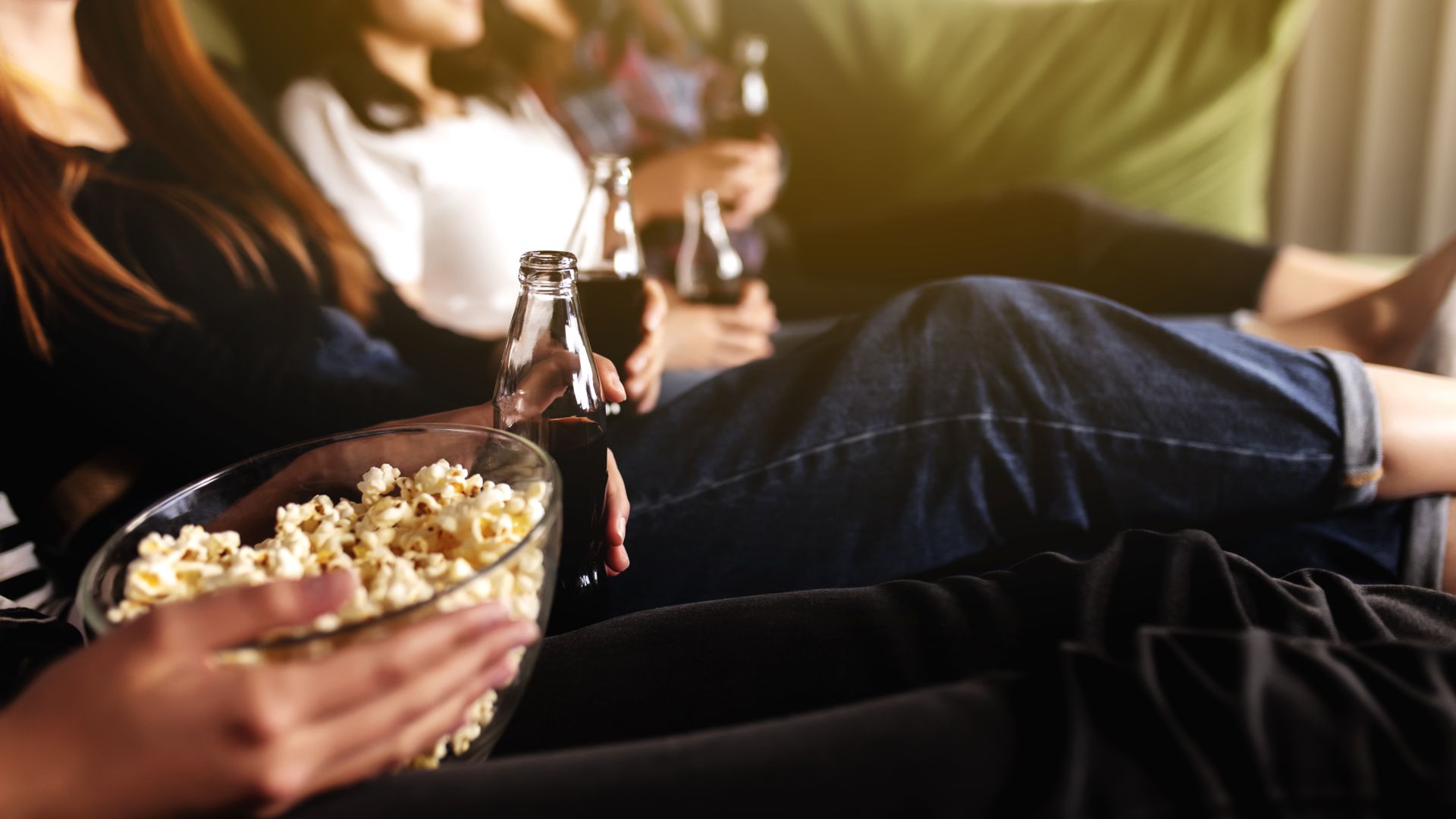 Friends relaxing together with popcorn and drinks while watching a film.