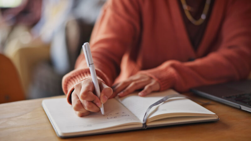 Girl in red jumper writing notes into a notepad. These can be used to enhance blogs created using AI.