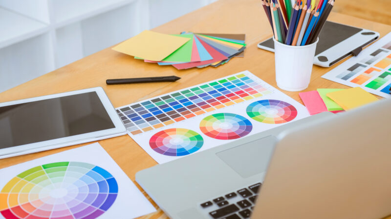 Lots of colour swatches laid out on table next to an open laptop.