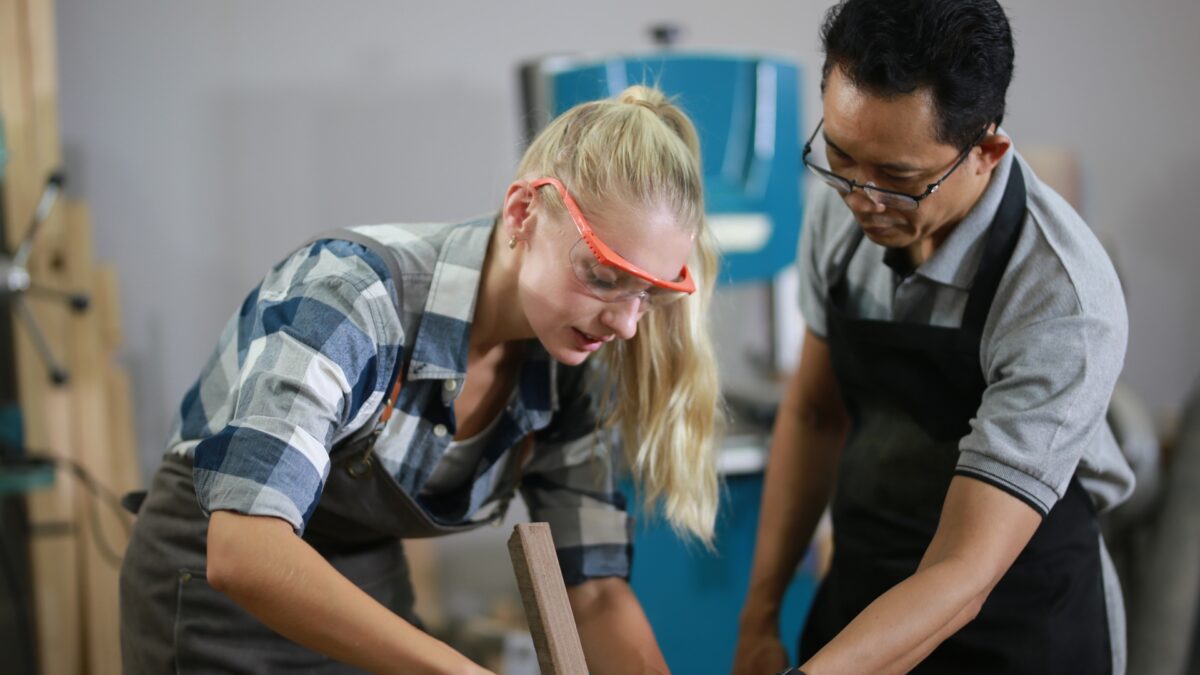 Craftsperson teaching apprentice woodworking skills representing human expertise guiding AI content creation