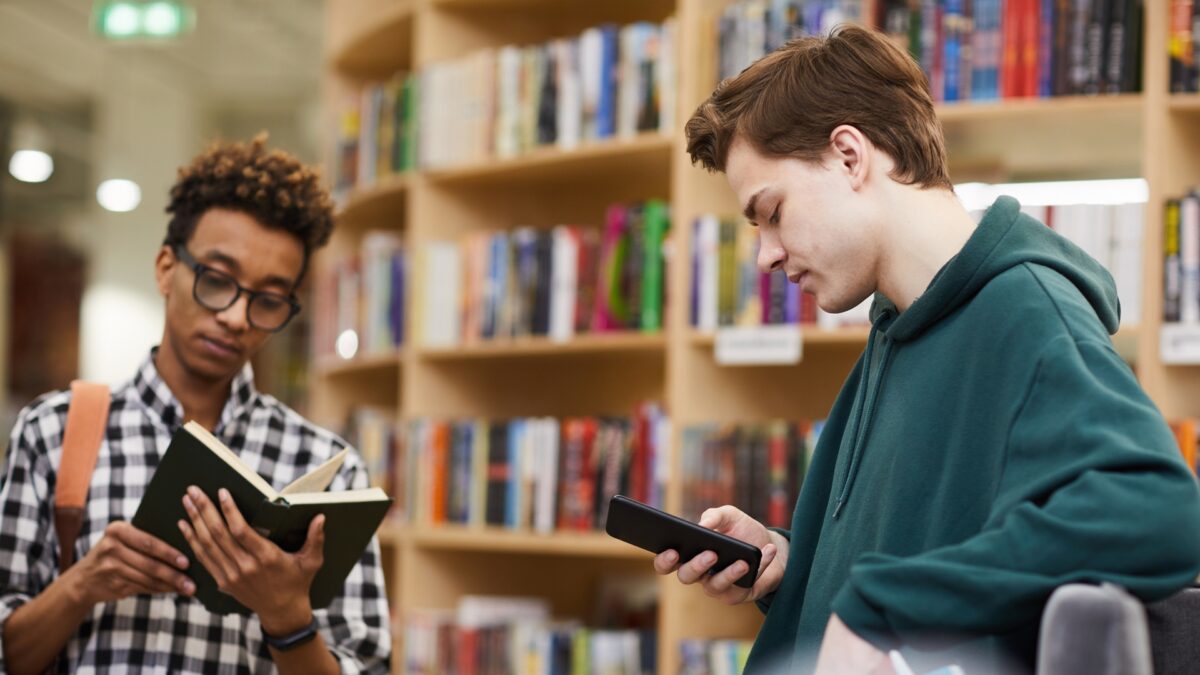 Young people comparing traditional reading and smartphone AI search research in a library environment near London